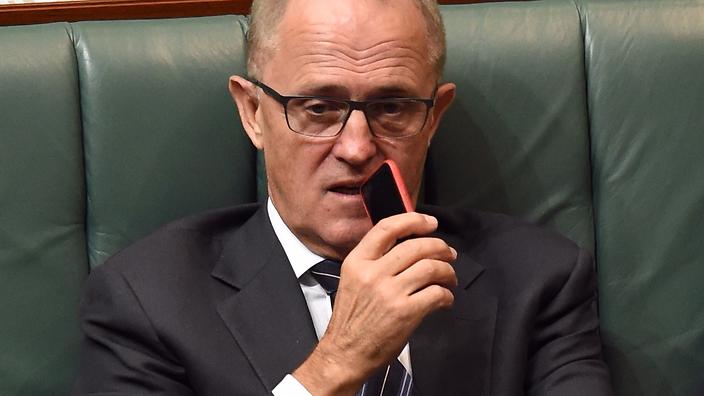 Communications minister Malcolm Turnbull holds his mobile phone up to his mouth as he listens and watches Question Time from the frontbench in the house of representatives at Parliament House in Canberra, Monday, Feb. 23, 2015. (AAP Image/Mick Tsikas) NO ARCHIVING