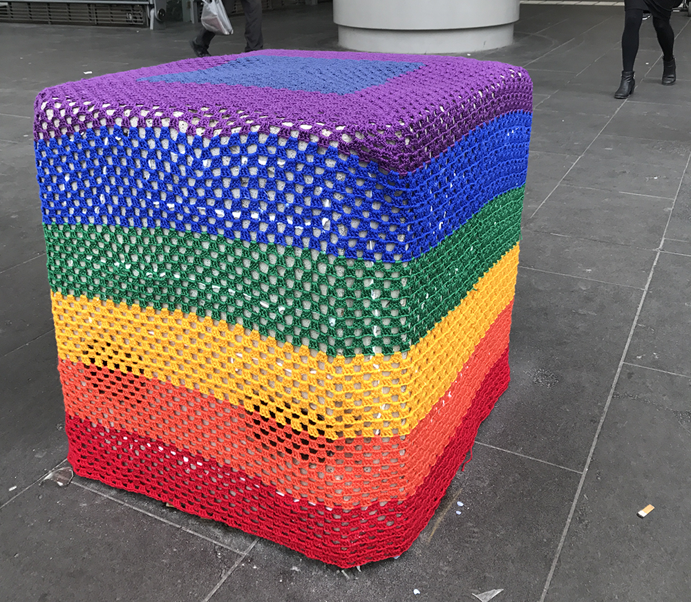 A crocheted rainbow flag covering a concrete bollard in Melbourne