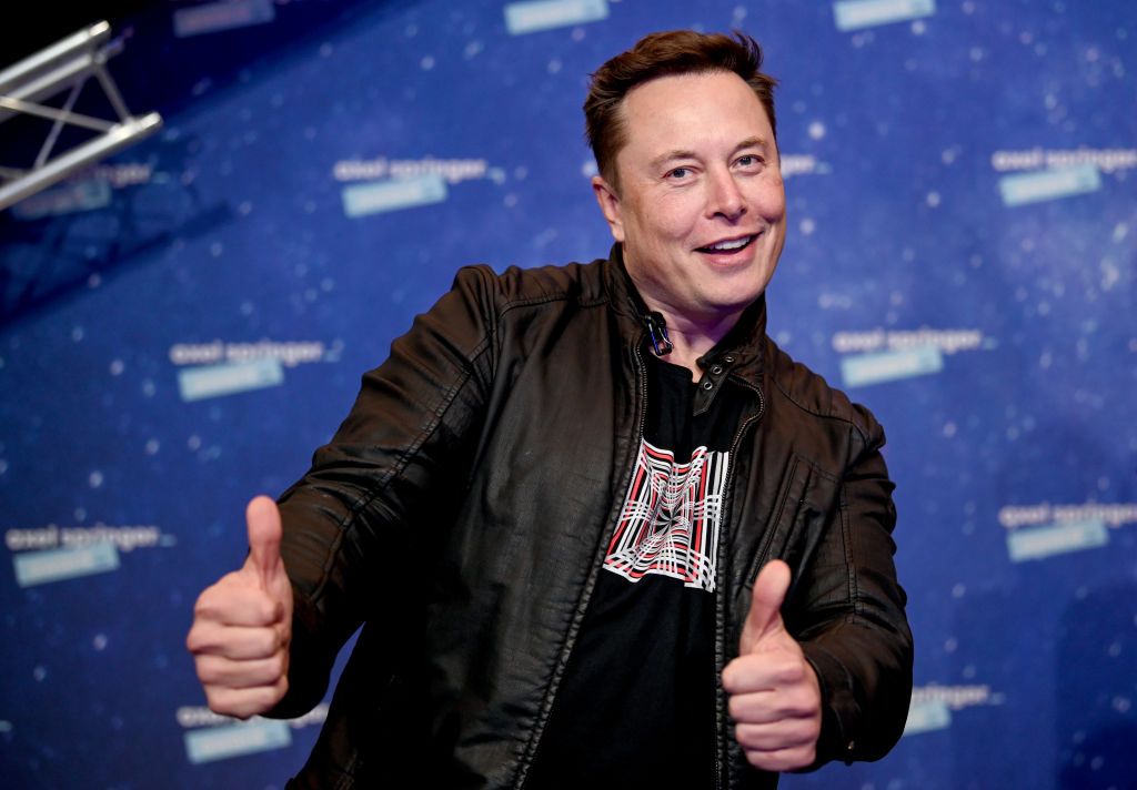 Elon musk wearing dark jacket and shirt giving two thumbs up to the camera