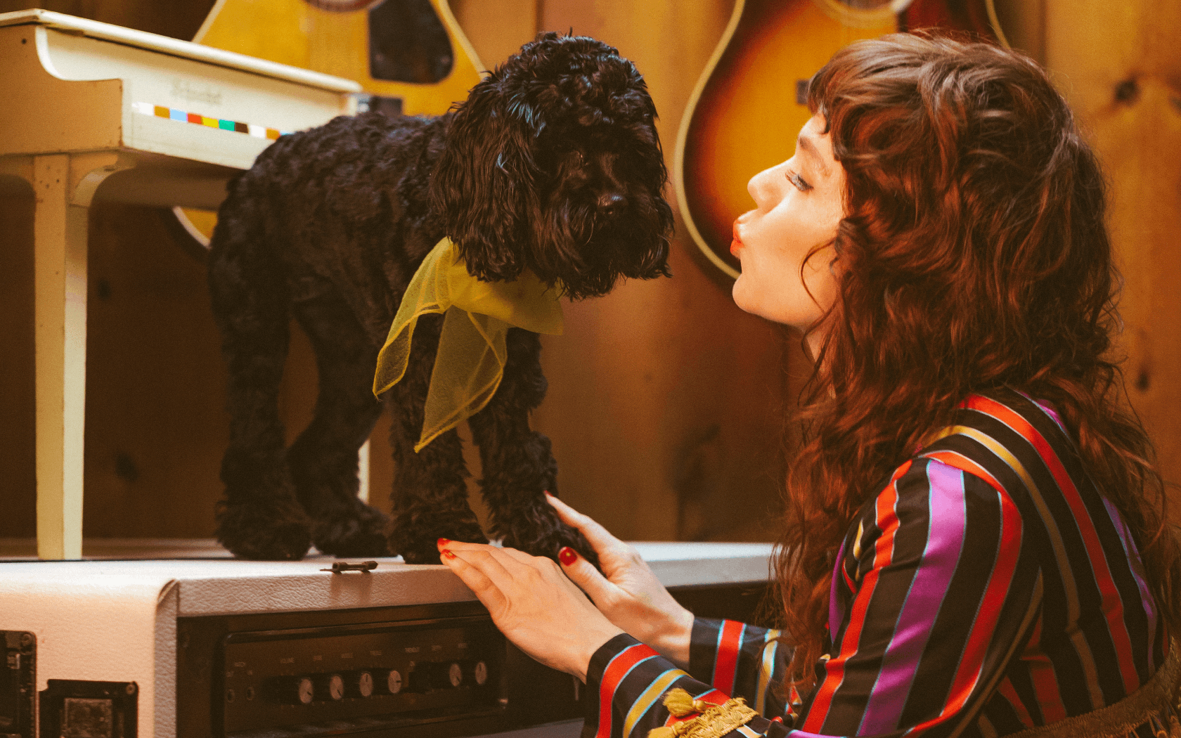 Jenny Lewis wearing a jacket and making a kissing gesture at a black puppy