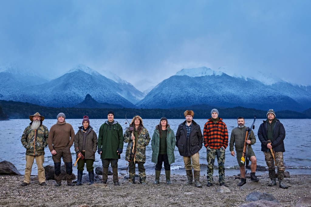the contestants of alone australia season 2 lined up on a lake beach with mountains in the background
